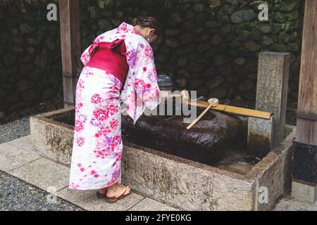 Kyoto, Japon - 15 septembre 2017 : une femme en kimono rinçant les mains à la fontaine d'eau purify japonaise, appelée chozubachi, au sanctuaire de Fushimi Inari Taisha Banque D'Images