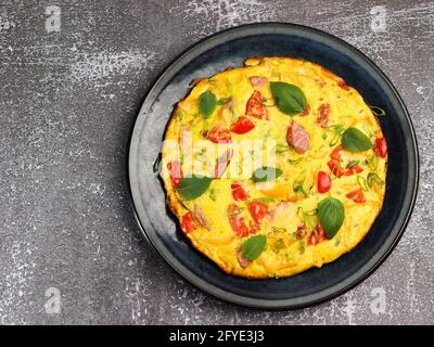 Omelette aux tomates, saucisse et poivron aux herbes sur une assiette ronde sur fond sombre. Vue de dessus, plan d'appartement Banque D'Images