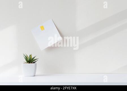 Composition avec un minimum d'objets sur un bureau blanc. Note carrée en papier blanc sur la table dans le bureau. Intérieur avec des ombrages abstraits pendant la journée ensoleillée. Banque D'Images