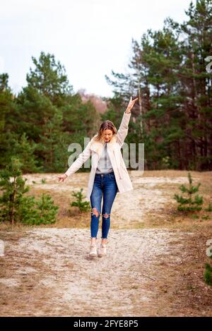 Jeune belle blonde longue cheveux femme debout vue de face avec les mains levées sur fond vert naturel extérieur. Jeune femme bras élevés appréciant Banque D'Images