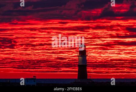 28 mai 2021, Mecklembourg-Poméranie occidentale, Warnemünde: Le soleil levant colore le ciel derrière le phare sur la jetée à la mer Baltique orange-rouge. Le Service météorologique allemand (DWD) présente son bilan météorologique pour le printemps. Photo: Jens Büttner/dpa-Zentralbild/dpa Banque D'Images