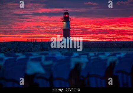 28 mai 2021, Mecklembourg-Poméranie occidentale, Warnemünde: Le soleil levant colore le ciel derrière le phare sur la jetée à la mer Baltique orange-rouge. Le Service météorologique allemand (DWD) présente son bilan météorologique pour le printemps. Photo: Jens Büttner/dpa-Zentralbild/dpa Banque D'Images