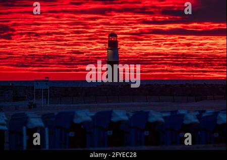 28 mai 2021, Mecklembourg-Poméranie occidentale, Warnemünde: Le soleil levant colore le ciel derrière le phare sur la jetée à la mer Baltique orange-rouge. Le Service météorologique allemand (DWD) présente son bilan météorologique pour le printemps. Photo: Jens Büttner/dpa-Zentralbild/dpa Banque D'Images