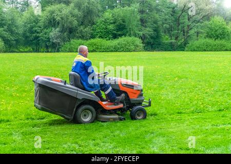 Un homme adulte travaillant dans un parc en uniforme tond une pelouse Banque D'Images