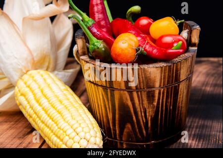 Épis de maïs avec piments et tomates légumes frais nourriture naturelle dans seau en bois, bio Banque D'Images