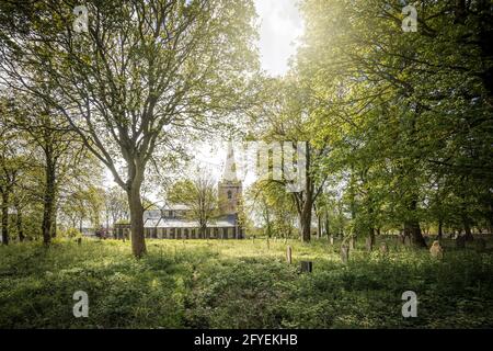 Belle vieille église catholique abandonnée dans un cimetière de chantier de cimetière surcultivé avec des pierres tombales victoriennes dans le domaine. Coucher de soleil à travers de grands arbres de long Banque D'Images