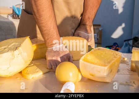 Les mains du commerçant coupent une tête de fromage en gros plan. Fromage artisanal dans un marché de rue. Fromager coupant du fromage dans son atelier. Fête de la gastronomie dans Banque D'Images