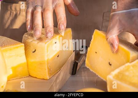 Les mains du commerçant coupent une tête de fromage en gros plan. Fromage artisanal dans un marché de rue. Fromager coupant du fromage dans son atelier. Fête de la gastronomie dans Banque D'Images