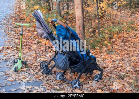 Deux poussettes vides se tenant à côté l'une de l'autre et un scooter dans un parc d'automne sans personnes. Le concept des enfants disparus. Banque D'Images