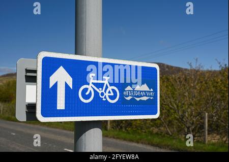 Panneau indiquant Hebridean Way cycle route. Texte, icône de vélo, flèche. Arrière-plan flou de la route Banque D'Images