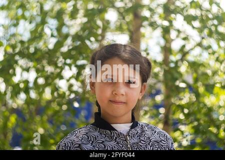 Fille de 8 ans contre arbre vert. Jour, prise de vue horizontale vue avant. Banque D'Images