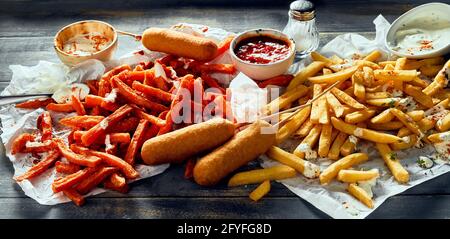 Préparation appétissante de frites rouges et classiques servies sur des mouchoirs avec des chiens de maïs délicieux avec des sauces à la tomate et à la crème Banque D'Images