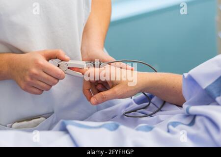 Infirmière avec un patient hospitalisé. Hôpital de Limoges, France, dosage de la saturation en oxygène-hémoglobine du sang avec un oxymètre de pouls. Banque D'Images