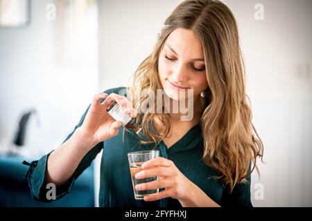 Femme versant des gouttes de macérate dans un verre d'eau. Banque D'Images