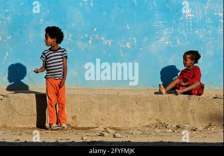 Deux enfants éthiopiens jouant, un garçon debout et une petite fille assise, devant une maison colorée dans le village d'Atsbi, Tigray, Ethiopie Banque D'Images