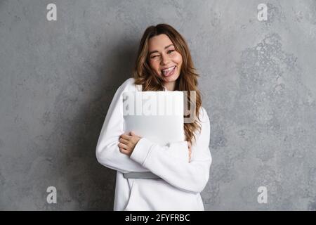 Bonne jeune femme excitée dans des vêtements décontractés tenant un ordinateur portable isolé sur un fond gris Banque D'Images