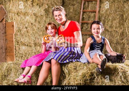 Mère et enfants bavarois assis sur grange avec bretzels Banque D'Images