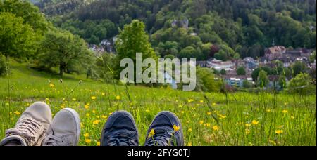 Deux paires de chaussures de randonnée pédestre sur le fond d'une belle montagne verte et vue sur une colline sur un village isolé. Profiter de la vue. Gros plan. Banque D'Images