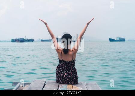 Une femme chinoise assise avec elle dos à la caméra À la fin de la jetée historique de Tan dans le Georgetown région de Penang Malaysia vue sur le Th Banque D'Images