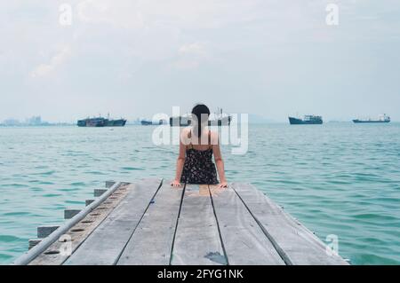 Une femme chinoise assise avec elle dos à la caméra Sur la jetée historique de Tan dans la région de Georgetown Penang Malaysia vue sur les détroits o Banque D'Images