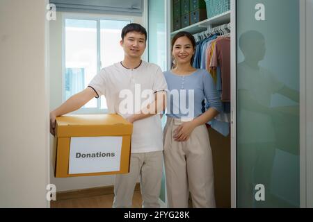 Les couples asiatiques sont debout près du placard des vêtements dans le dressing portant une boîte de vêtements donnés à apporter au centre de dons. Banque D'Images