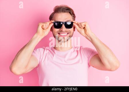 Photo de joli charmant jeune gentleman habillé décontracté t-shirt bras lunettes sombres sourire isolé couleur rose fond Banque D'Images