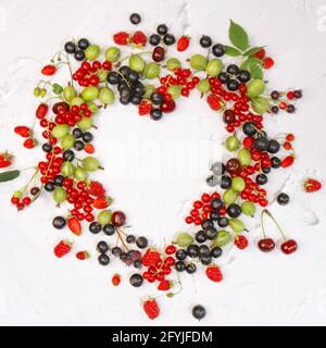 Les groseilles d'été, les framboises et les groseilles à maquereau sont en forme de coeur sur fond blanc. Bordure de baies. Vue rapprochée du dessus ou plan de travail à plat avec pla Banque D'Images