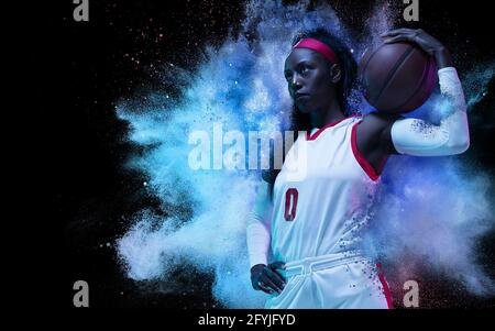 Une jeune femme sportif joueur de basket-ball dans l'explosion de couleur poudre de néon isolée sur fond sombre Banque D'Images