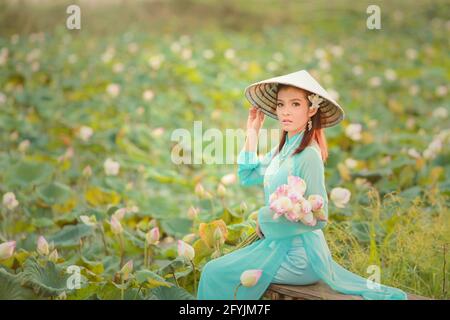 Portrait d'une belle femme dans un chapeau conique traditionnel tenant un bouquet de fleurs de nénuphars, Thaïlande Banque D'Images