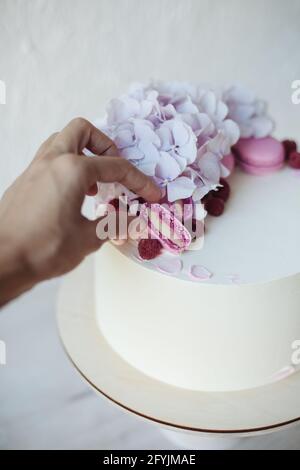 Femme décorant un gâteau éponge de crème de beurre avec un macaron rose Banque D'Images