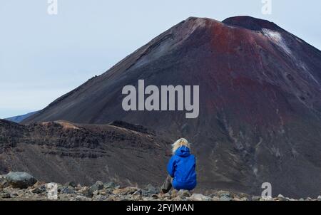 Vue arrière d'une femme assise sur un rocher qui regarde le volcan, Parc national de Tongariro, Île du Nord, Nouvelle-Zélande Banque D'Images