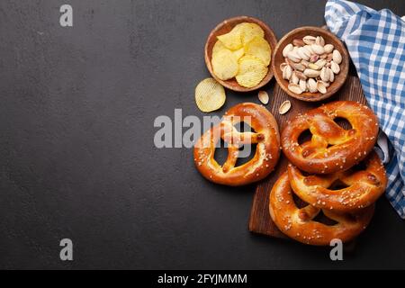 Chips de pommes de terre, pistaches et bretzel maison frais cuit avec sel de mer sur table en pierre. Collation classique à la bière. Vue de dessus du plan de travail avec espace de copie Banque D'Images