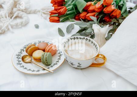 Tasse de café et assiette de macarons à côté d'un bouquet de tulipes Banque D'Images