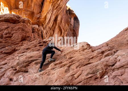 Une femme qui escalade sur le rocher pour atteindre le sommet du parc national d'Arches à Moab, Utah Banque D'Images