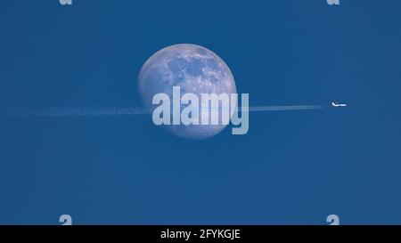 Gros plan de la lune gibbeuse à la cire pendant la journée contre un ciel clair de blus. Un Ariplane traverse la lune et laisse un sentier de condensation derrière - S. Banque D'Images