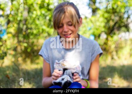 Flou blonde petite fille souriante jouant avec chat, noir et blanc petit chaton. Nature flou vert d'été arrière-plan. Une fille qui s'en est à l'animal. J'adore Banque D'Images