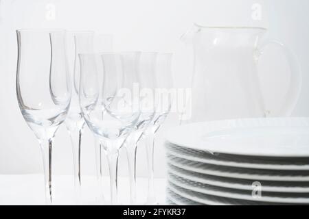 Jeu de plaques empilées, de verres en cristal et d'une verseuse en verre sur une table blanche. Banque D'Images