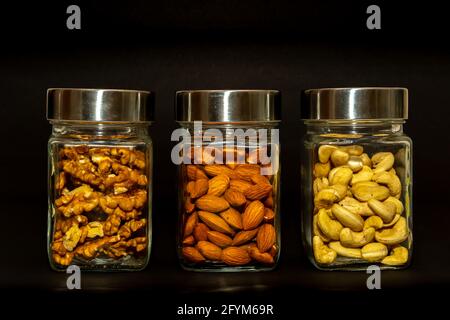 Pots en verre remplis de noix, noix de cajou et amandes sur fond noir Banque D'Images