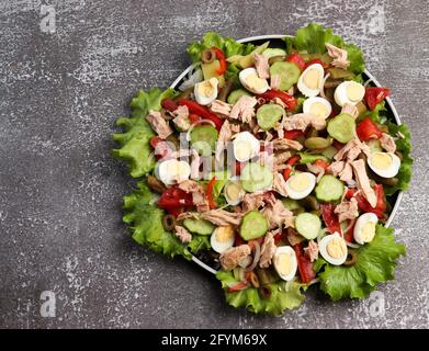 Salade niçoise au thon, concombres, poivrons, oignons, œufs de caille, haricots et pommes de terre sur une plaque ronde sur fond sombre. Vue de dessus, plan d'appartement Banque D'Images