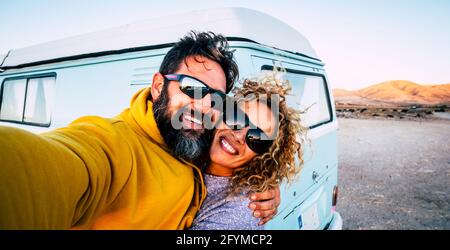 Un couple d'adultes heureux sourit et s'amuse ensemble en prenant le selfie image avec l'ancienne fourgonnette classique vintage en arrière-plan - concept de vanlife et de voyage personnes Banque D'Images