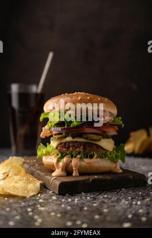 restauration rapide. un grand hamburger juteux avec patty de bœuf, laitue iceberg, tomates, cornichons, oignons et sauce et tranches de bacon. Touche basse, ambiance sombre Banque D'Images