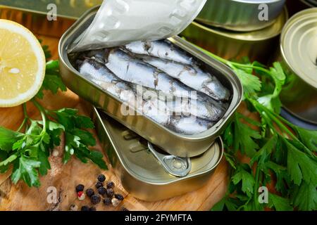 Vue rapprochée de l'ouvert peut de sardines fumées dans l'huile sur table en bois avec du persil frais, de citron et d'épices Banque D'Images