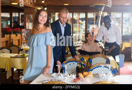 Gentilhomme aidant jeune femme attrayante avec sa chaise dans le restaurant Banque D'Images