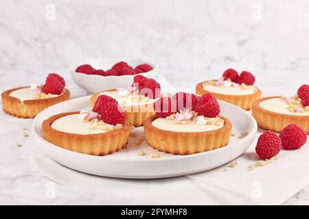 Tartelettes à la crème blanche, nappées de fruits à la framboise et de saupoudrés d'amande sur une assiette blanche Banque D'Images