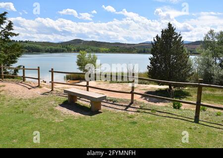 Vue sur le parc de la Grajera depuis une aire de loisirs. Banc, clôture en bois, pins et lac. Banque D'Images