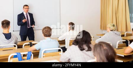 Homme enseignant avec bloc-notes donne des cours intéressants pour les étudiants dans la salle de classe Banque D'Images