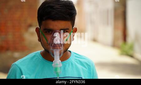 Jaipur, Inde - Mai 2021: Jeune homme infecté par la maladie de Corona virus. Patient inhalant de l'oxygène porter un masque avec un flux d'oxygène liquide. Concept hôpital Banque D'Images