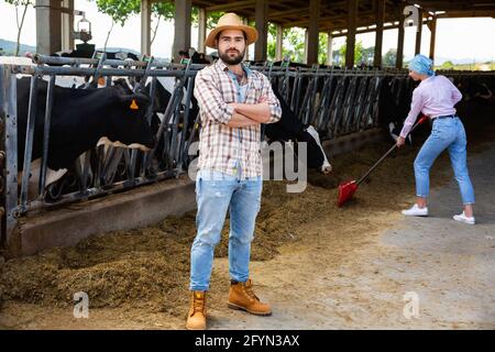 Confiant jeune heureux joyeux souriant homme propriétaire de ferme laitière debout en arrière-plan avec un troupeau de vaches Banque D'Images