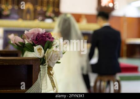 Fleurs roses décoratives avec arrière-plan flou de bride et de marié à l'église lors d'une cérémonie de mariage Banque D'Images