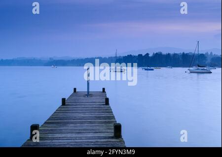 Vue depuis la petite jetée en bois sur Windermere (bateaux sur l'eau calme, promenade, lumière bleue spectaculaire du soir) - Lake District, Cumbria, Angleterre Royaume-Uni. Banque D'Images